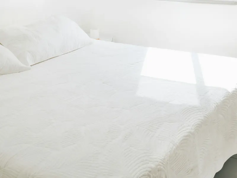 Sunlight falling across a neatly made bed with white linens
